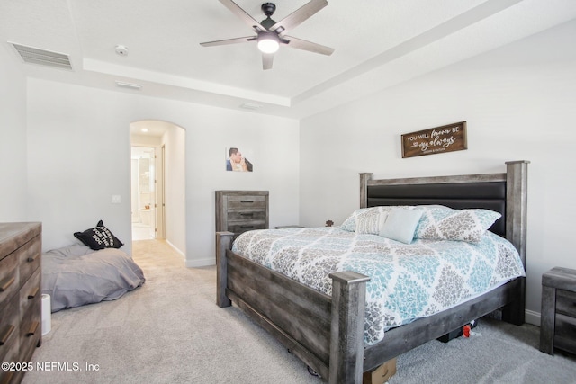 bedroom with baseboards, visible vents, arched walkways, light colored carpet, and a tray ceiling