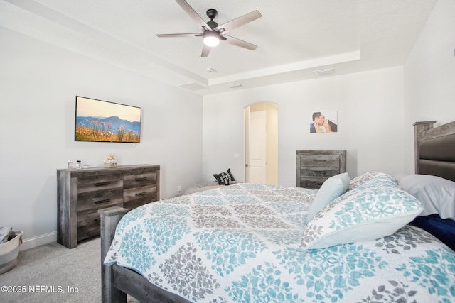 bedroom with light carpet, a raised ceiling, a ceiling fan, and baseboards