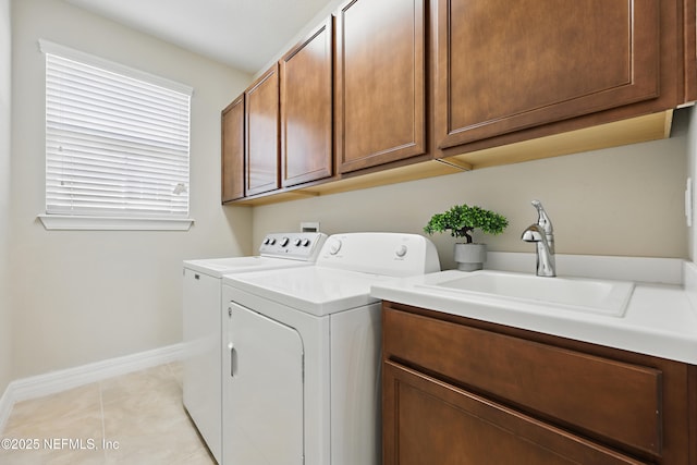 clothes washing area featuring light tile patterned floors, washing machine and dryer, a sink, baseboards, and cabinet space