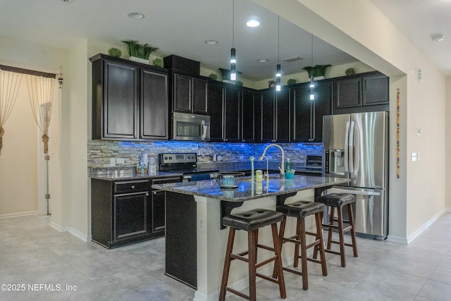 kitchen with appliances with stainless steel finishes, a sink, dark cabinetry, and a kitchen breakfast bar