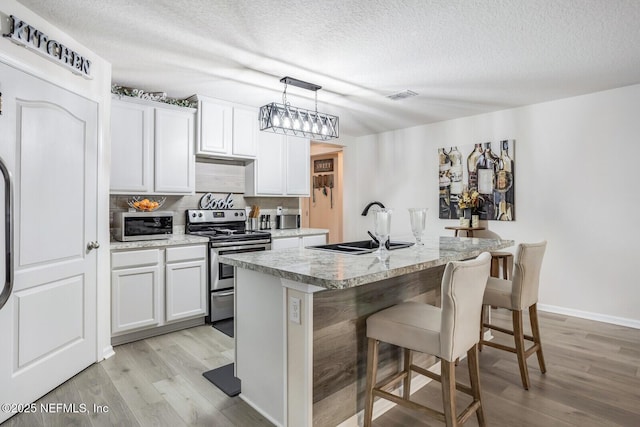 95170 Timberlake Dr, Fernandina Beach, FL 32034 - kitchen with white cabinets, an island with sink, stainless steel electric stove, light countertops, and a sink