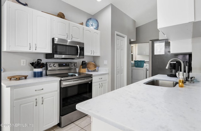 kitchen featuring light tile patterned flooring, a sink, white cabinets, washer and dryer, and appliances with stainless steel finishes