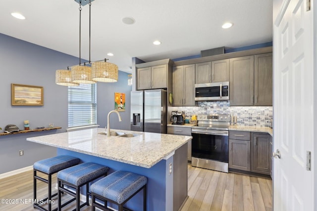 kitchen with light stone counters, a sink, appliances with stainless steel finishes, light wood finished floors, and tasteful backsplash