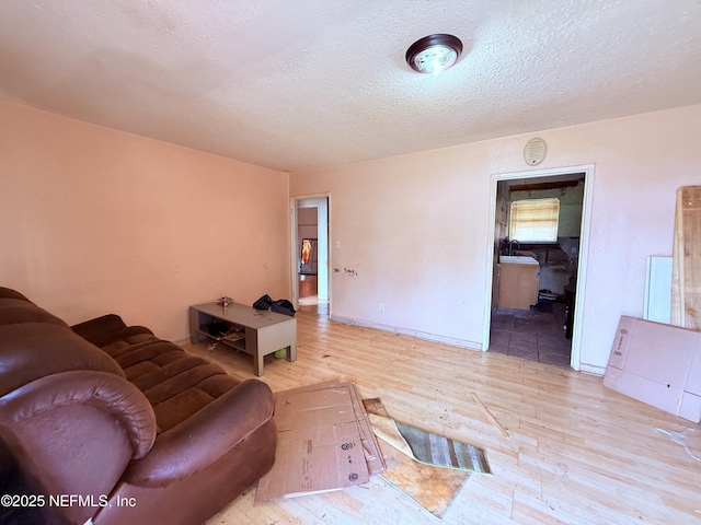 living room with baseboards, a textured ceiling, and light wood finished floors