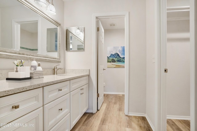 bathroom with a walk in closet, wood finished floors, vanity, and baseboards