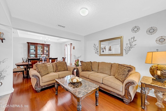 living area with visible vents, wood finished floors, baseboards, a textured ceiling, and a notable chandelier