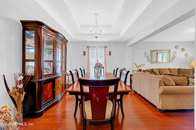 dining area with wood finished floors, a textured ceiling, a chandelier, and a tray ceiling