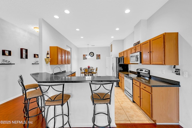 kitchen with a peninsula, dark countertops, a kitchen breakfast bar, recessed lighting, and appliances with stainless steel finishes