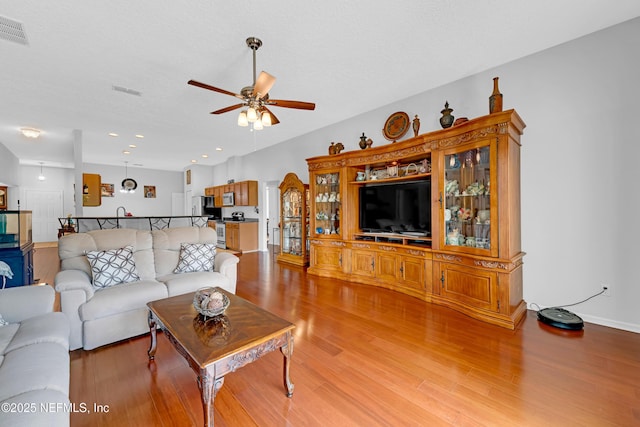 living room featuring ceiling fan, visible vents, light wood-type flooring, baseboards, and recessed lighting