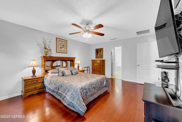 bedroom with a textured ceiling, baseboards, visible vents, and wood finished floors