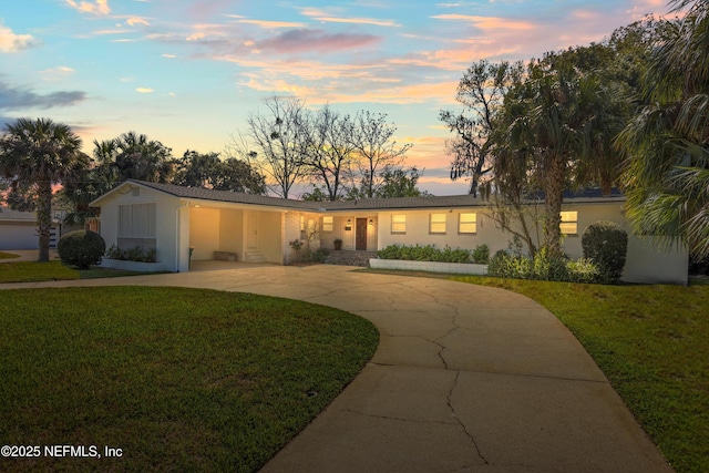 ranch-style house featuring concrete driveway, a yard, and stucco siding