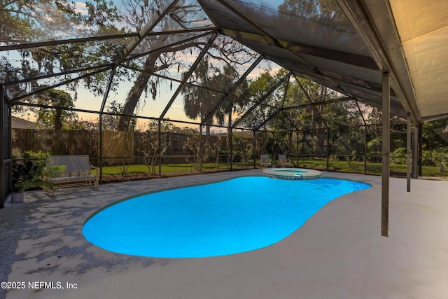 pool at dusk with glass enclosure, a patio area, a pool with connected hot tub, and fence