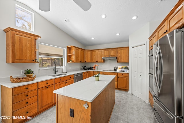 kitchen featuring appliances with stainless steel finishes, brown cabinetry, vaulted ceiling, a sink, and a kitchen island