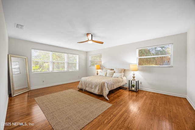 bedroom with ceiling fan, wood finished floors, visible vents, and baseboards