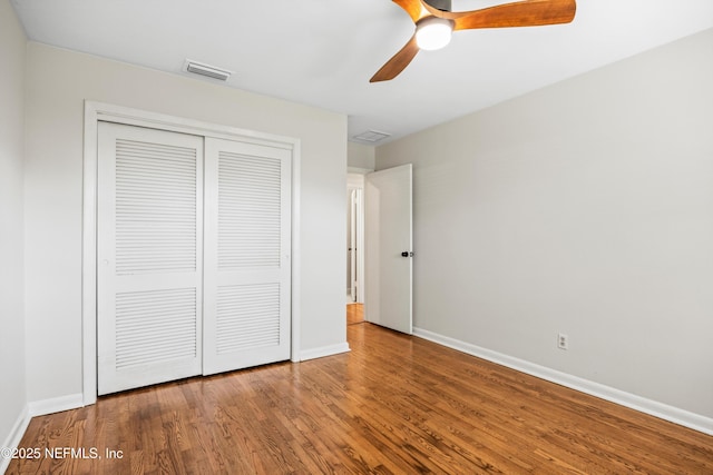 unfurnished bedroom with a closet, visible vents, a ceiling fan, wood finished floors, and baseboards