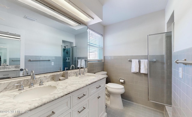 bathroom featuring toilet, a stall shower, tile walls, and a sink