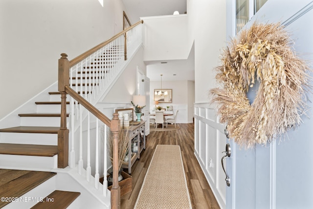 foyer entrance featuring a chandelier, a high ceiling, wood finished floors, stairs, and wainscoting