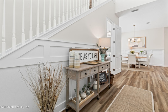 hallway featuring a wainscoted wall, visible vents, a decorative wall, wood finished floors, and a chandelier