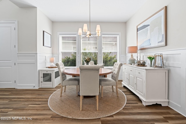 dining space featuring an inviting chandelier, a decorative wall, dark wood finished floors, and wainscoting