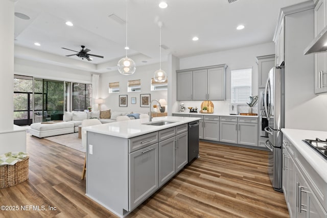 kitchen featuring dark wood-style flooring, a sink, a kitchen island with sink, gray cabinetry, and stainless steel dishwasher