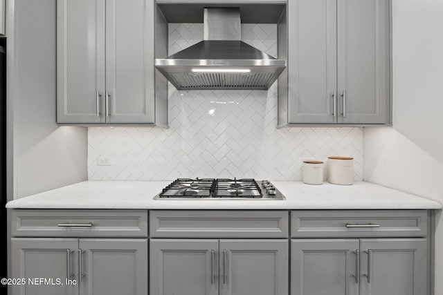 kitchen with decorative backsplash, wall chimney exhaust hood, light countertops, gray cabinetry, and stainless steel gas stovetop