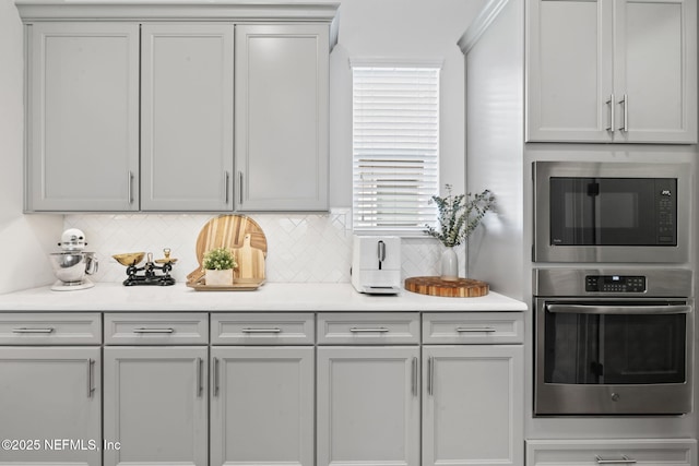 kitchen with appliances with stainless steel finishes, decorative backsplash, light countertops, and gray cabinetry