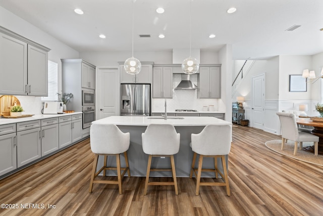 kitchen featuring wall chimney range hood, gray cabinets, stainless steel appliances, and a sink