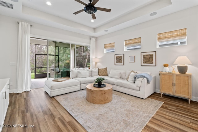 living area featuring dark wood-type flooring, a tray ceiling, visible vents, and baseboards