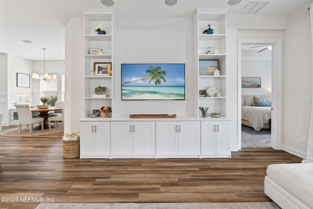 living area with built in shelves, dark wood-type flooring, visible vents, and a notable chandelier