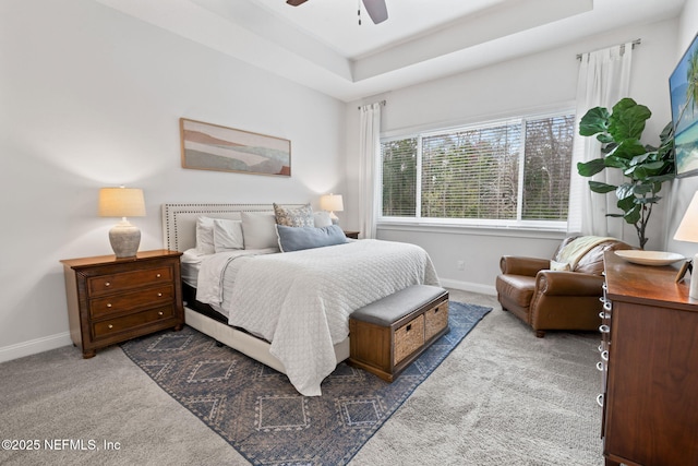 carpeted bedroom with ceiling fan, a tray ceiling, and baseboards