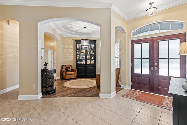 entrance foyer with ornamental molding, tile patterned flooring, french doors, and baseboards