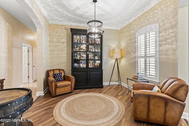 living area featuring ornamental molding, arched walkways, baseboards, and wood finished floors