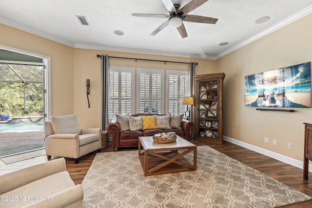 living area featuring visible vents, dark wood-type flooring, ornamental molding, a textured ceiling, and baseboards