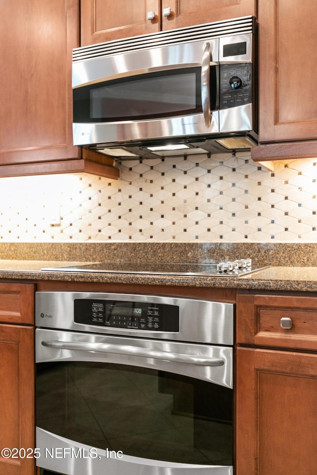 kitchen with appliances with stainless steel finishes, dark countertops, brown cabinetry, and tasteful backsplash