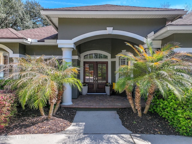 doorway to property featuring french doors, roof with shingles, and stucco siding