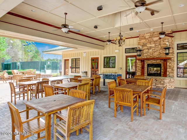 dining room featuring a ceiling fan, an outdoor stone fireplace, and wooden walls