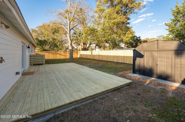 deck with a storage shed, a fenced backyard, a lawn, and an outbuilding