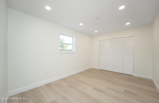 unfurnished bedroom with baseboards, a textured ceiling, light wood-style floors, a closet, and recessed lighting