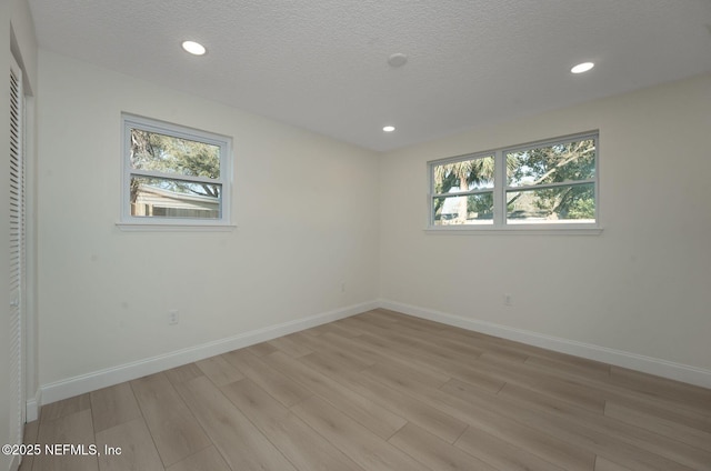 unfurnished room with light wood finished floors, baseboards, a textured ceiling, and recessed lighting