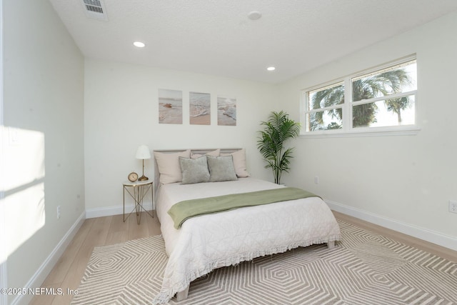 bedroom with a textured ceiling, light wood-style flooring, recessed lighting, visible vents, and baseboards