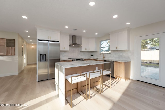 kitchen with stainless steel appliances, wall chimney exhaust hood, light countertops, and white cabinets