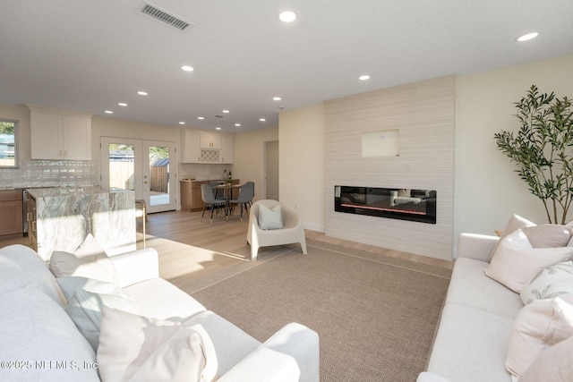 living area featuring a healthy amount of sunlight, light wood finished floors, a glass covered fireplace, and french doors