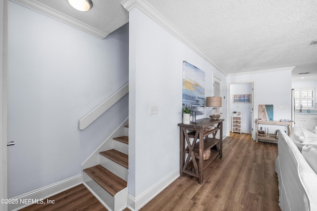 staircase featuring crown molding, visible vents, a textured ceiling, wood finished floors, and baseboards