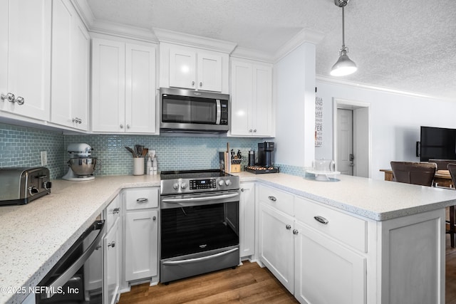 kitchen featuring a peninsula, wood finished floors, white cabinets, hanging light fixtures, and appliances with stainless steel finishes