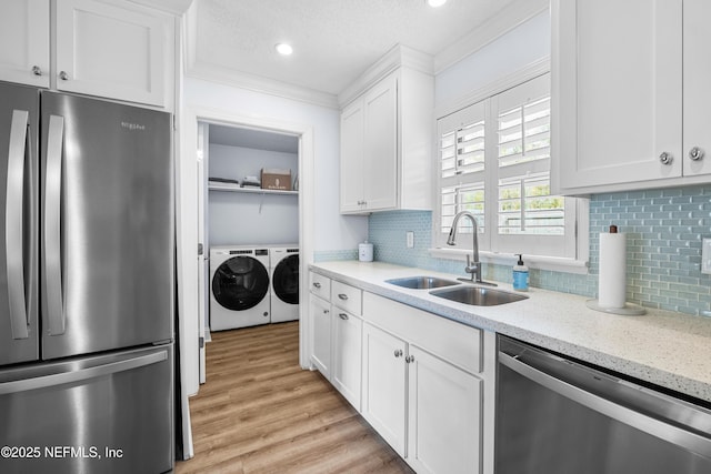 kitchen featuring stainless steel appliances, washing machine and dryer, white cabinets, a sink, and light stone countertops