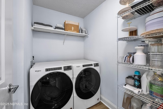 clothes washing area with a textured ceiling, laundry area, wood finished floors, baseboards, and washer and dryer