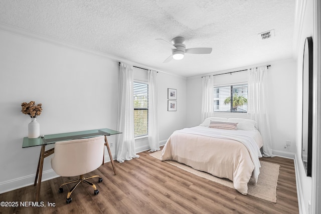 bedroom featuring baseboards, a textured ceiling, visible vents, and wood finished floors