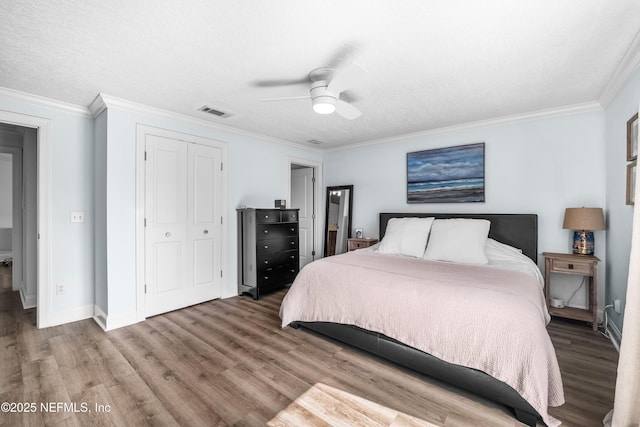 bedroom with a closet, visible vents, wood finished floors, and ornamental molding