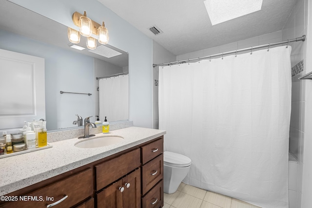 full bath featuring a textured ceiling, toilet, a skylight, vanity, and visible vents