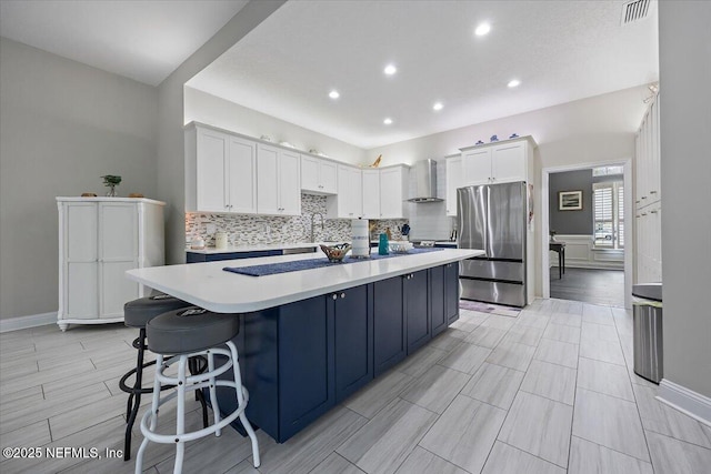 kitchen with white cabinets, light countertops, freestanding refrigerator, decorative backsplash, and wall chimney exhaust hood